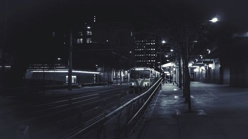 Illuminated railroad tracks by buildings in city at night