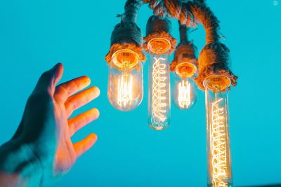 Low angle view of illuminated light bulbs against blue sky