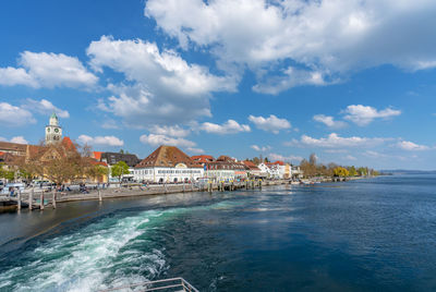 Buildings by sea against cloudy sky