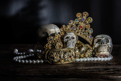 Close-up of human skulls and gold jewelry on table against black background