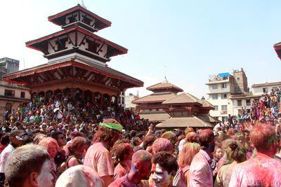 People celebrating holi at durbar square against sky