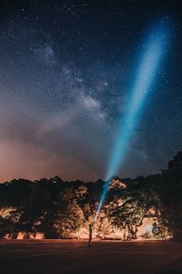 Man standing by mountain with flashlight towards star field at night