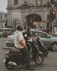Rear view of man riding motorcycle on street against buildings