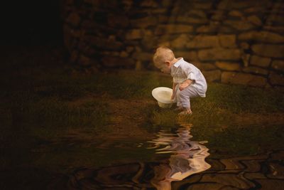Full length side view of boy holding hat with reflection in water