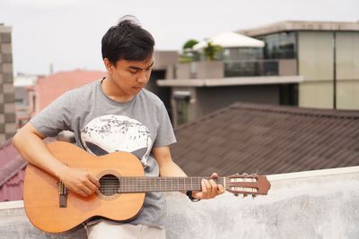 Man playing guitar while leaning on wall