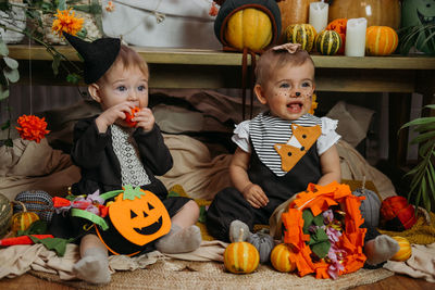 Two cute baby girl dressed in halloween costume sitting on bed with halloween decoration at home
