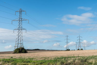 Electricity pylons on field against blue sky