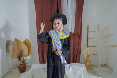 Portrait of smiling young woman standing against wall