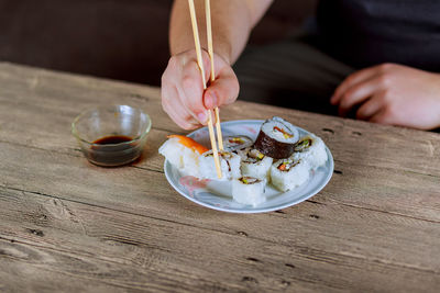 Cropped hands of child eating sushi on wooden table