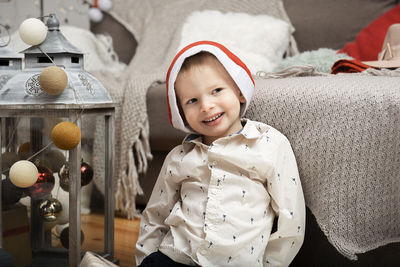 Portrait of  smiling boy child wearing a christmas hat sitting among  holiday decorations at home