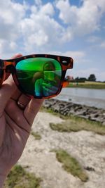 Cropped image of hand holding sunglasses against sky