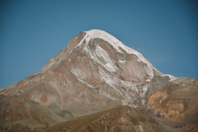 Low angle view of snowcapped mountain against clear blue sky