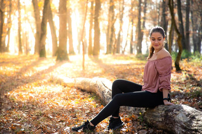 Smiling young woman sitting on fallen tree trunk in forest