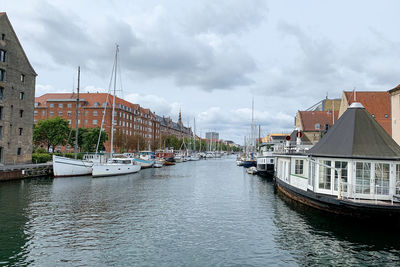 Sailboats moored on river by buildings against sky