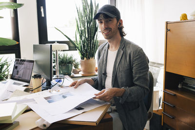 Portrait of male architect sitting with blueprint at desk in home office