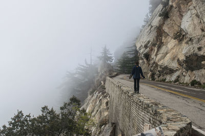 Rear view of person walking at the edge of mountain road
