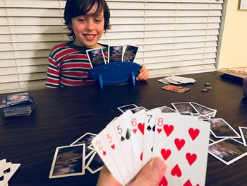 Boy playing cards with person on table