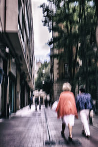 Rear view of people walking on footpath in city