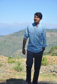 Full length of a young guy walking in hilly area with hand on pocket and looking away