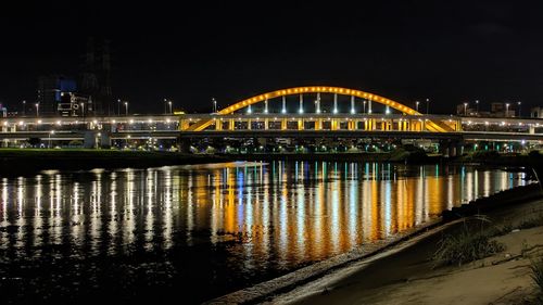 Illuminated bridge over river against sky at night