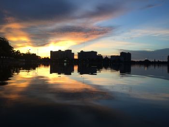 Buildings by river against sky during sunset