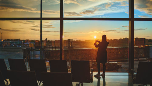 View on the aiport window with woman walking with suitcase at the departure hall during the sunset.