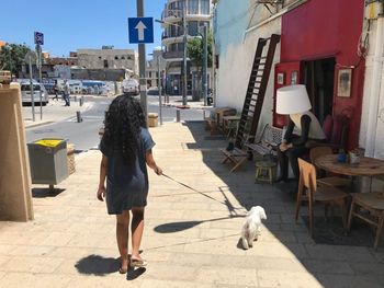 Rear view of woman with dog walking on footpath in city