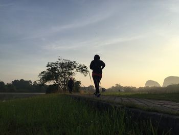 People jogging on footpath against sky during sunset