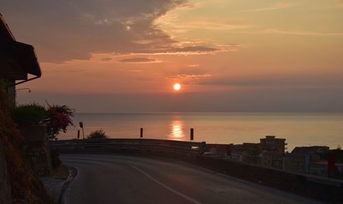 Road by sea against sky during sunset