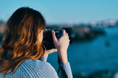 Rear view portrait of woman photographing sea