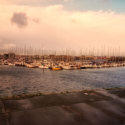 Sailboats moored on harbor against sky during sunset