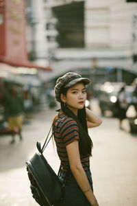 Portrait of young woman wearing cap while standing on road in city