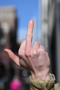 Cropped hand of man showing obscene gesture in city