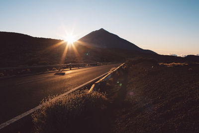 Road by mountains against sky during sunset