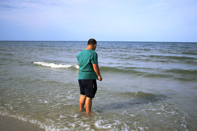 Man standing in sea on shore against sky