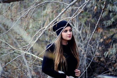 Beautiful woman looking away while standing by bare trees