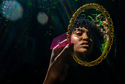 Young woman holding mirror in forest during sunny day