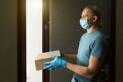 Man holding paper bag with food in doors, in medical gloves and protective mask, copy space. safe