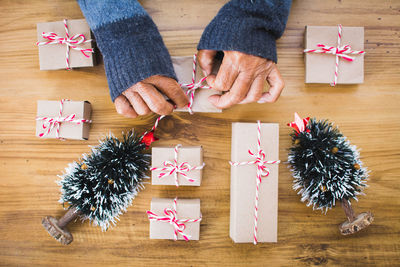 Cropped hands of man tying christmas presents on wooden table