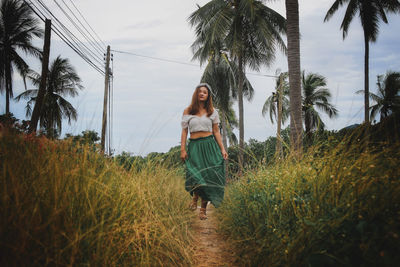 Woman standing by palm trees on field against sky