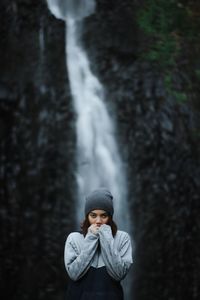 Portrait of young woman standing against waterfall