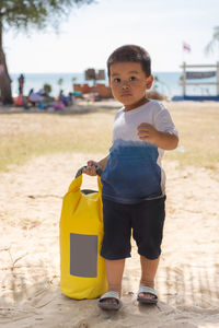 Portrait of cute boy holding bag while standing at beach