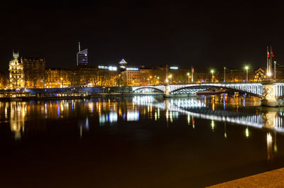 Illuminated bridge over river by buildings against sky at night