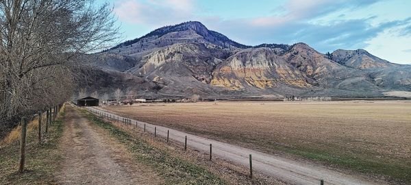 Dirt road by mountains against sky