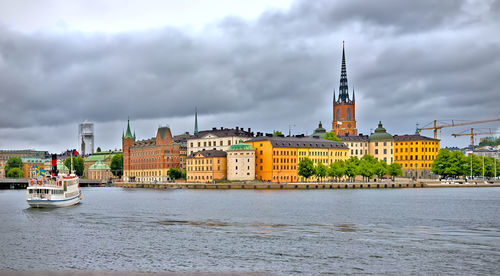 Buildings by river against cloudy sky