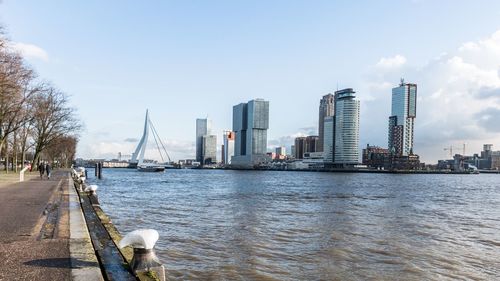 Bridge over river by buildings in city against sky