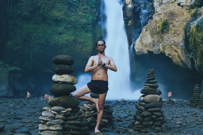 Full length of young woman standing against waterfall