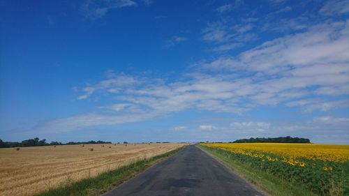 Road passing through agricultural field against sky