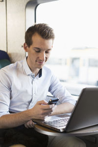 Young businessman using cell phone on train
