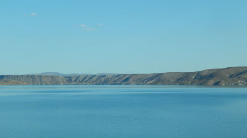 Scenic view of sea and mountains against clear blue sky